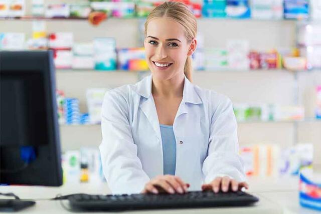 A female pharmacist smiles as she works on her computer | 900x600