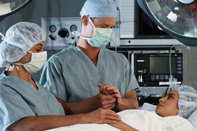 Doctors standing over female patient in bed and comforting before surgery